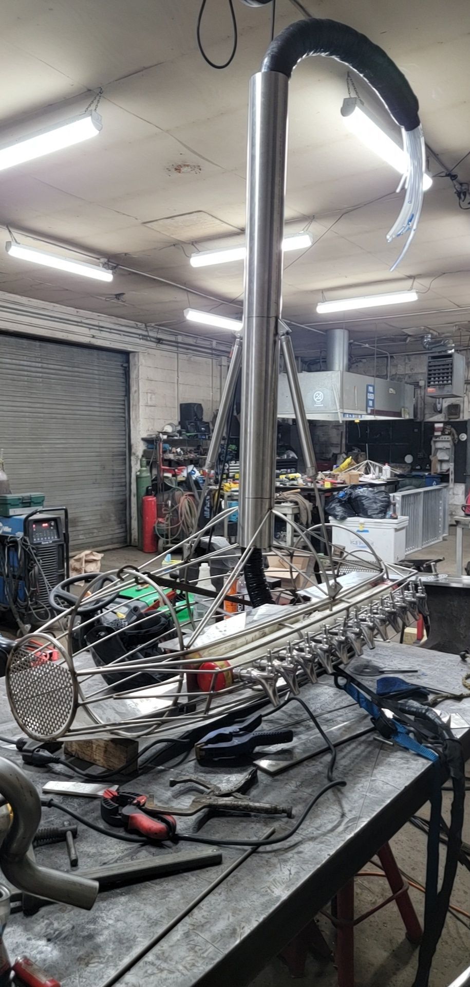 A workshop scene with a custom-built stainless steel device on a cluttered workbench.