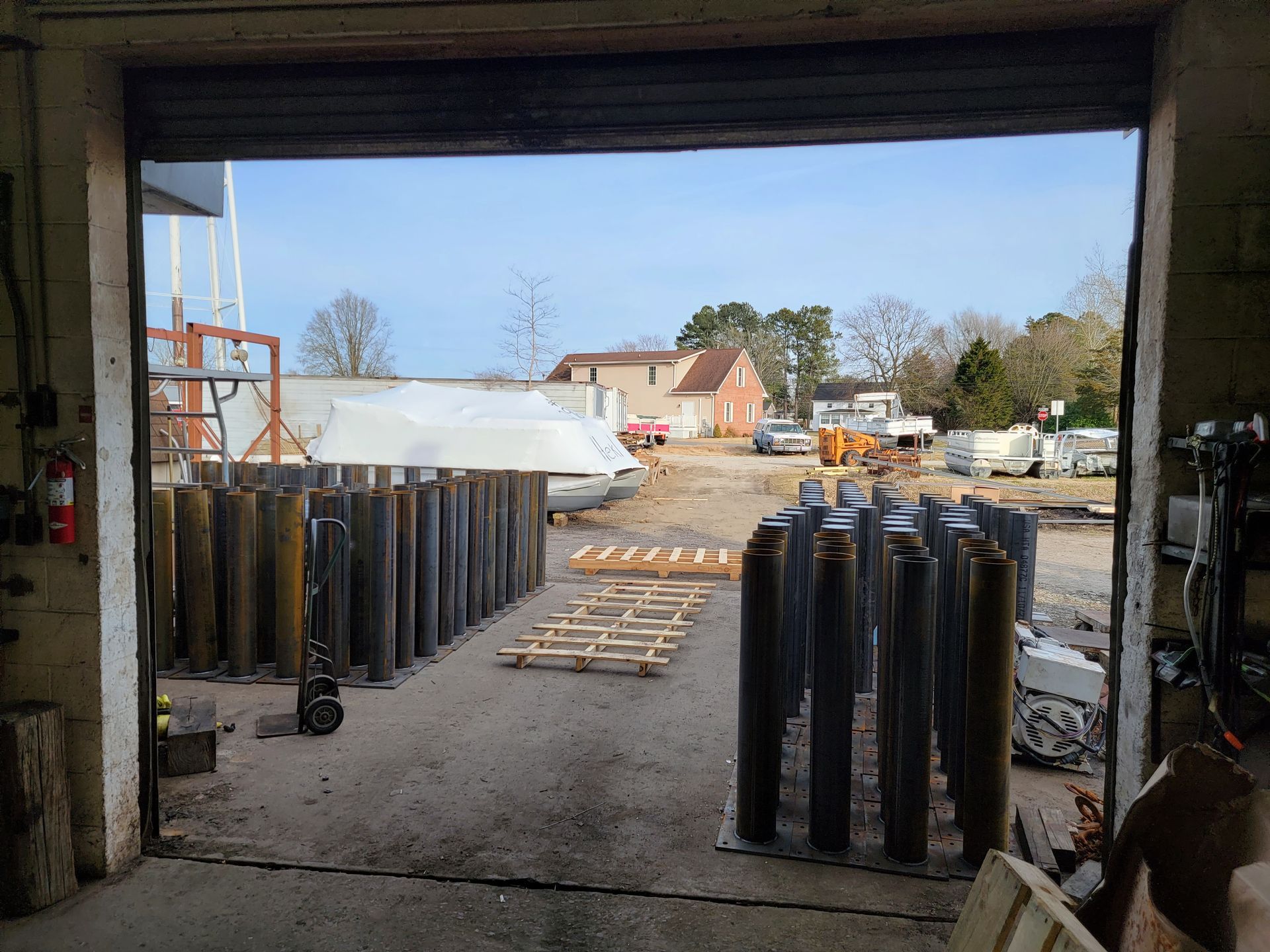 View from a warehouse opening, revealing a yard with cylindrical metal objects and a building under construction.