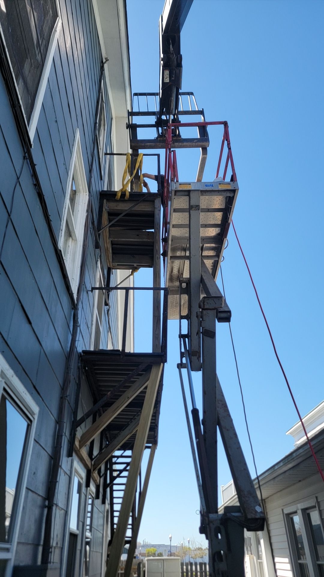 A tall black lift platform next to a building, providing access to its side. Sunny day.