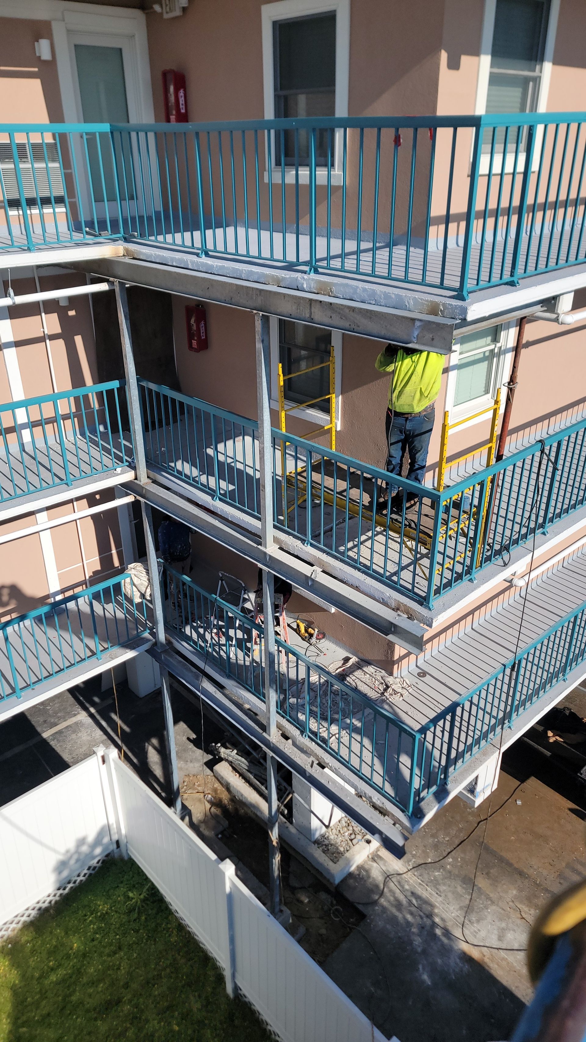 Building with teal balconies; worker on scaffolding.