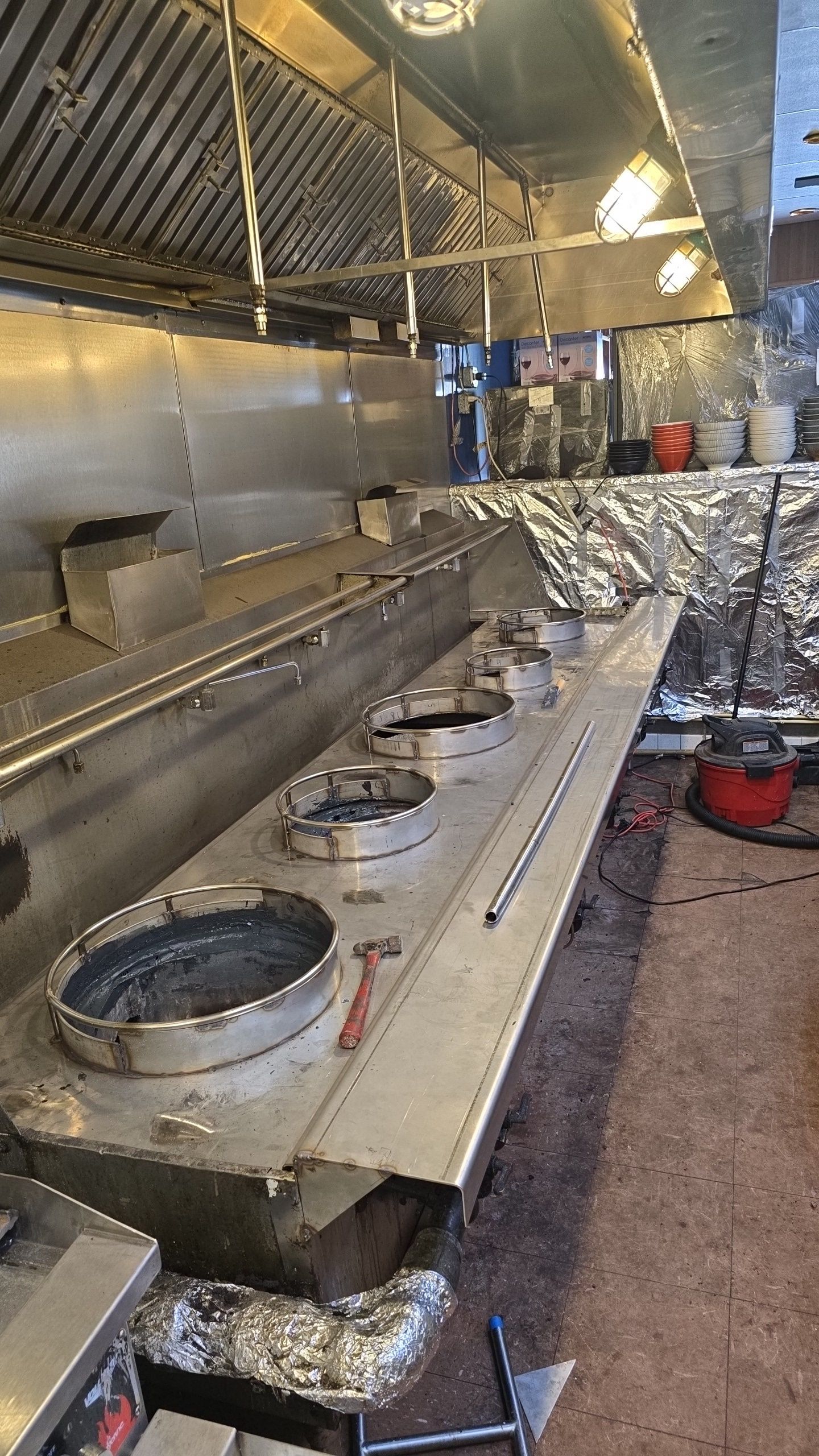 Stainless steel kitchen wok station with three burners under an exhaust hood.