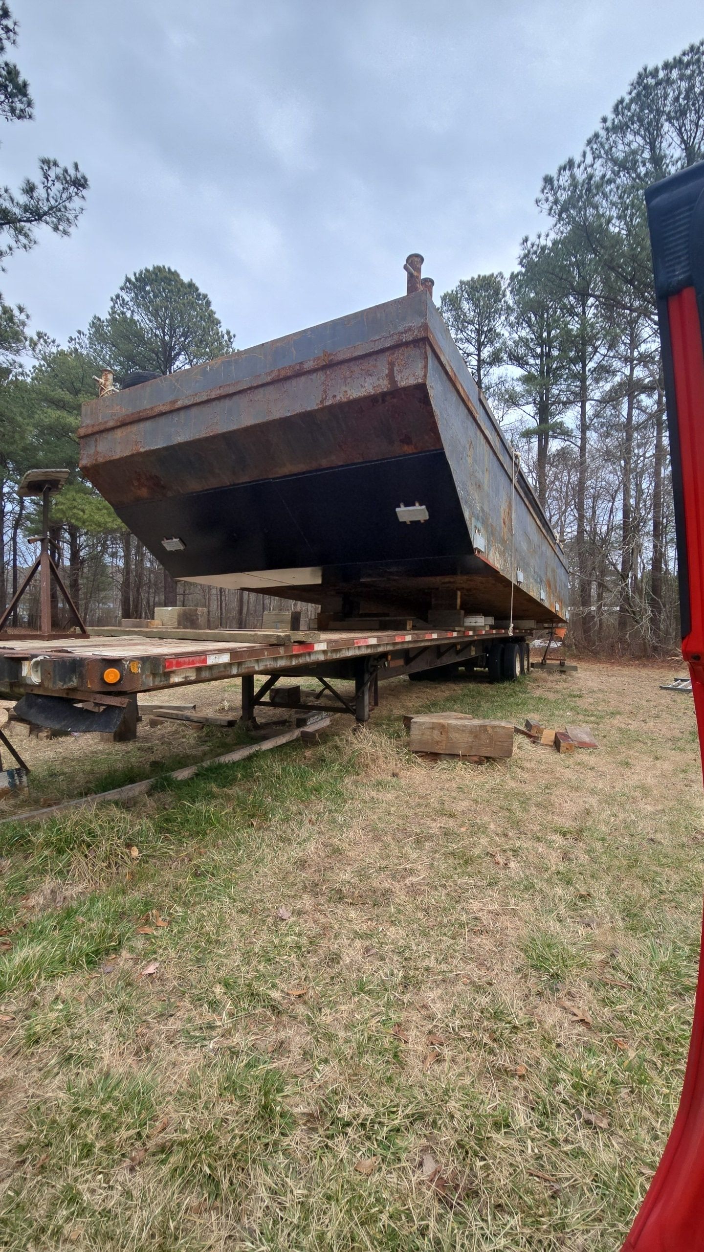A large, rusted dump trailer is tilted, ready to unload. It rests on a flatbed trailer in a field.