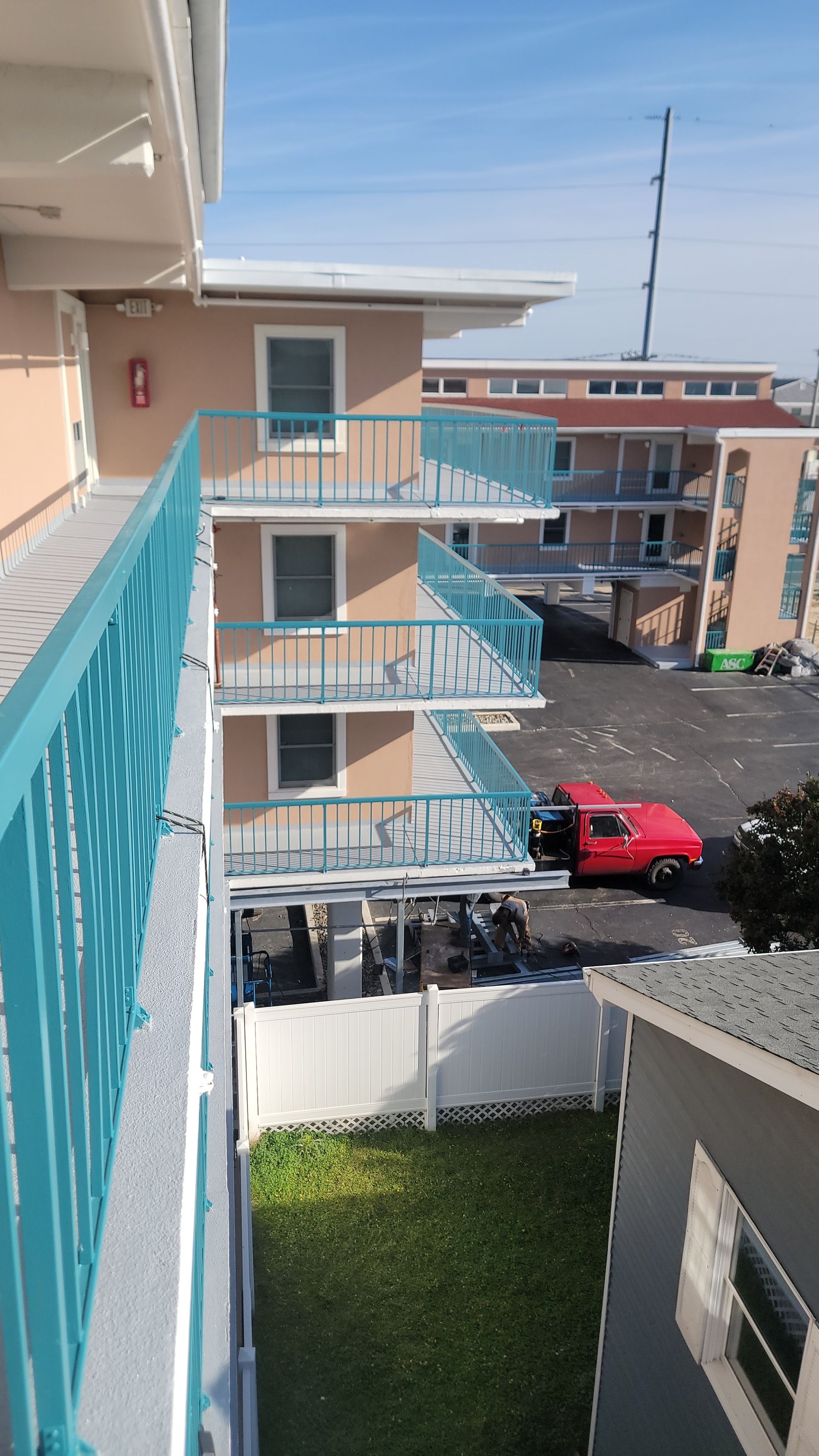 Three-story motel building with teal balconies. A red car is parked below.