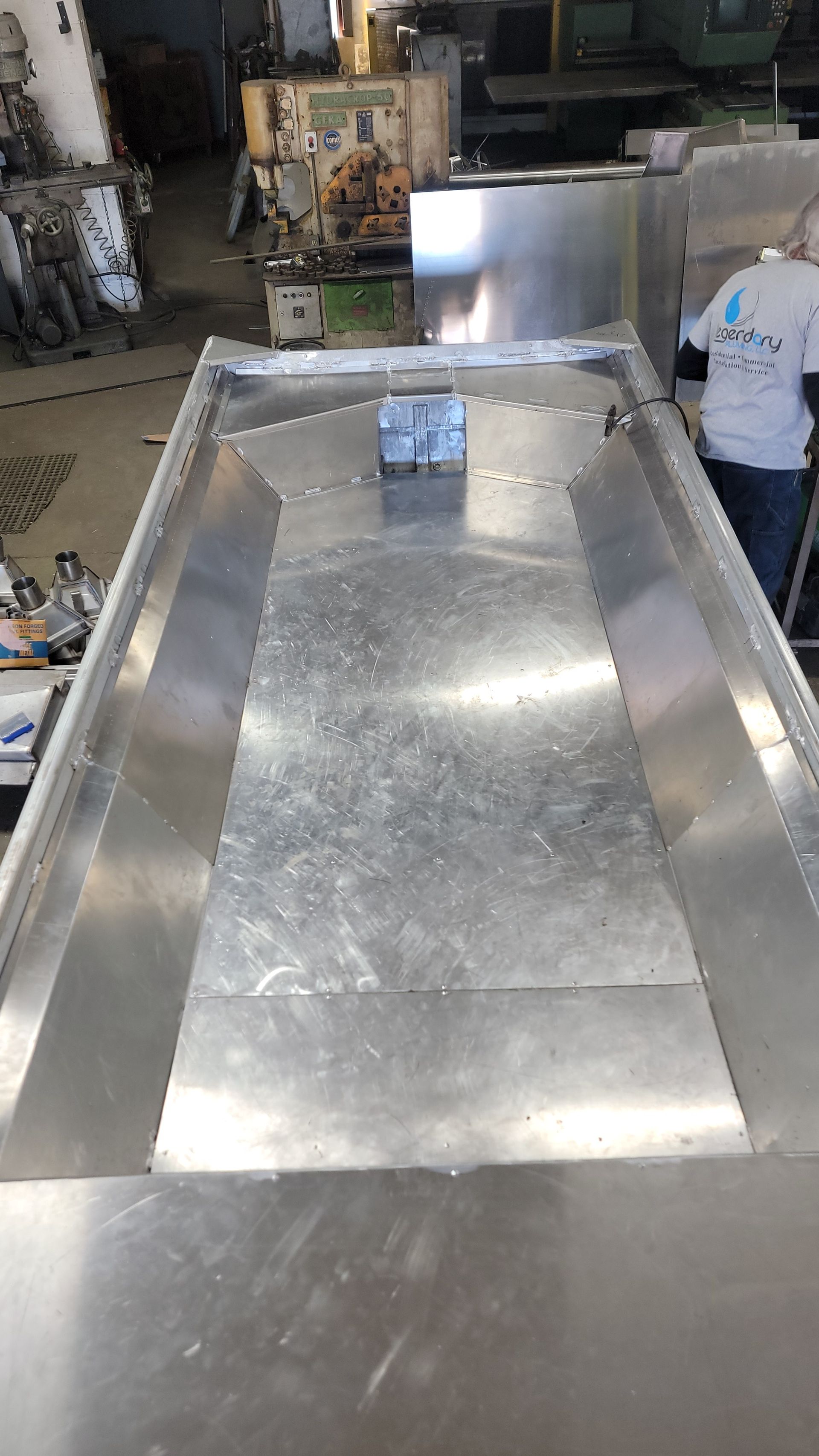 Large, stainless steel trough in a workshop; a person stands nearby.