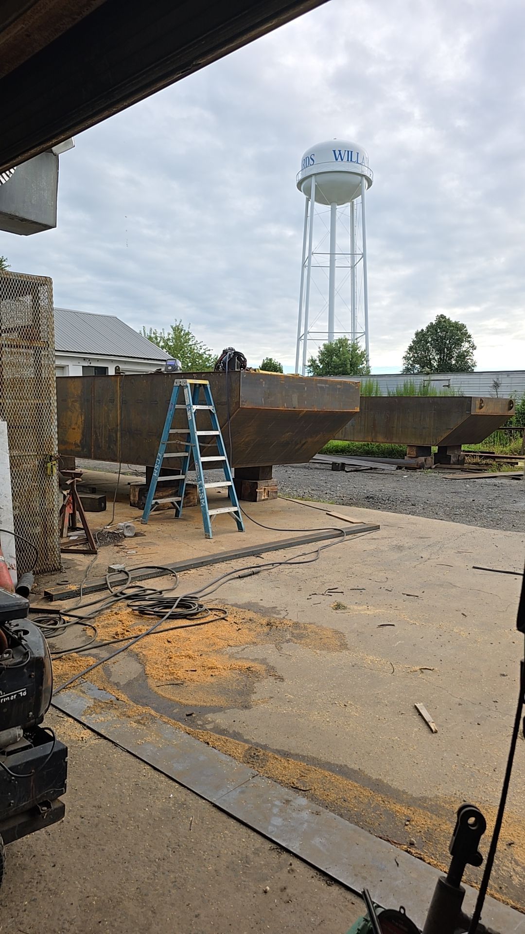 Steel structure construction site with ladder, water tower in background.