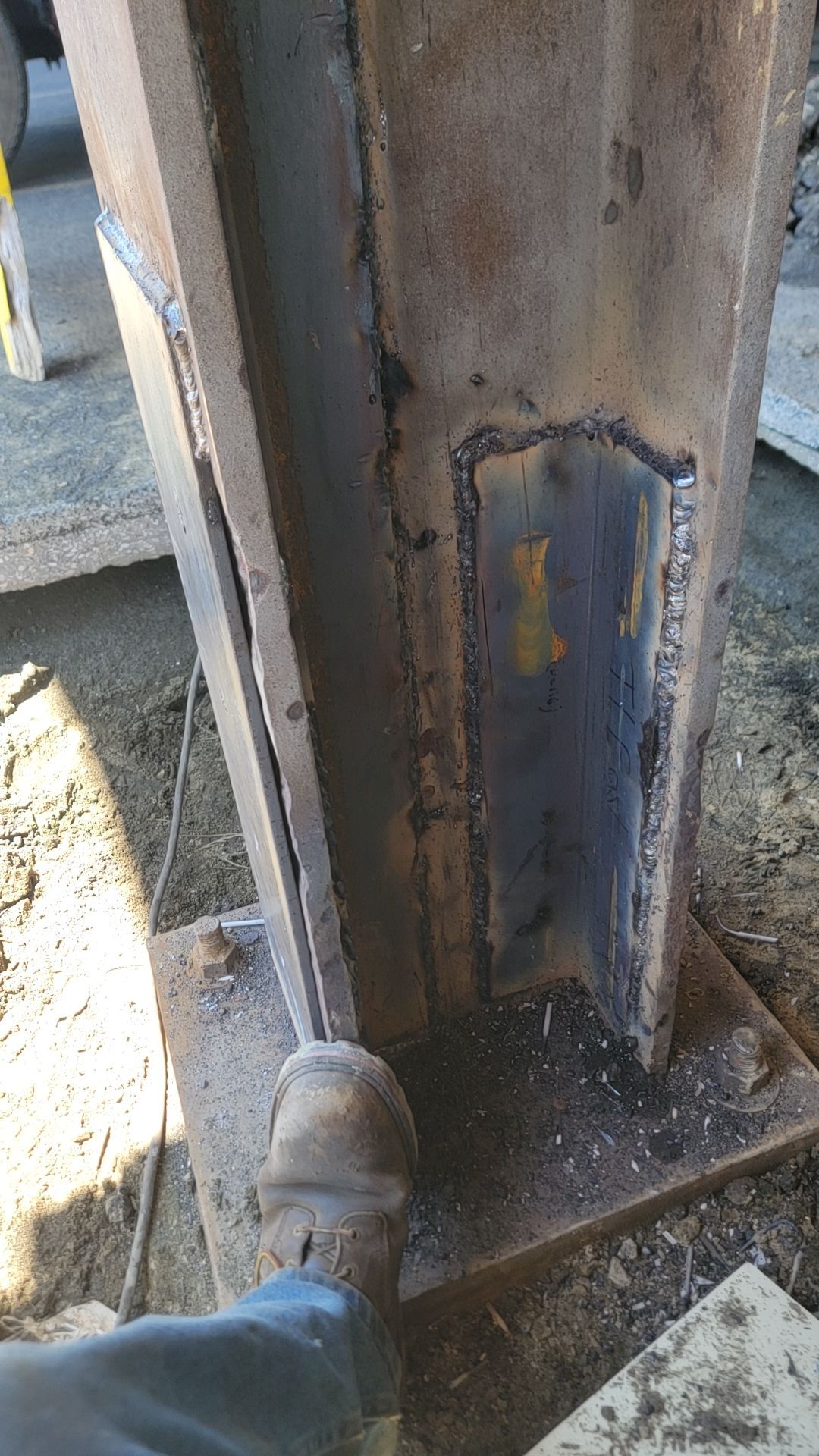 Welded steel beam with a boot visible. Construction site setting.