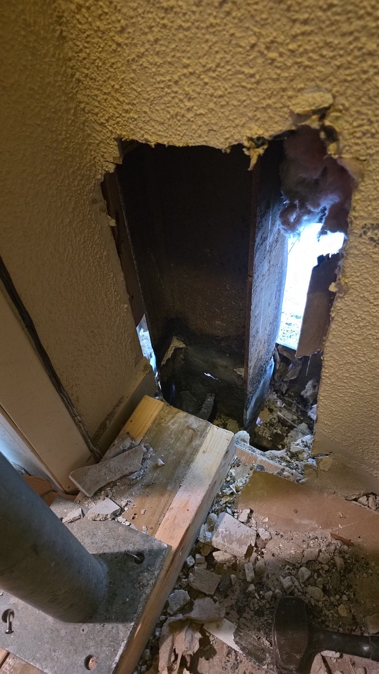 Hole in wall exposing interior; debris on floor, metal supports visible, daylight shines through.