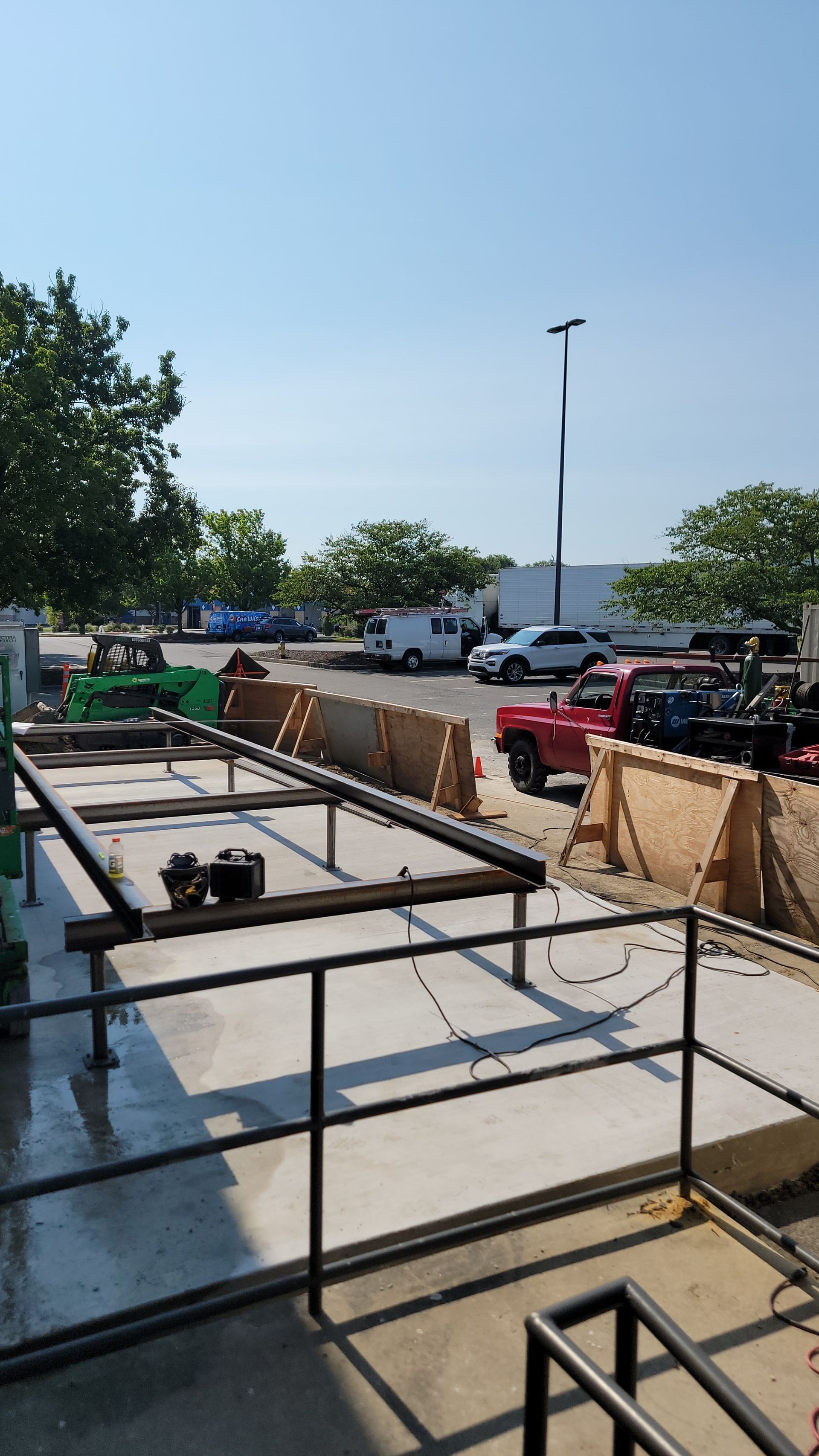 Construction site with concrete platform, metal framing, and vehicles under a blue sky.
