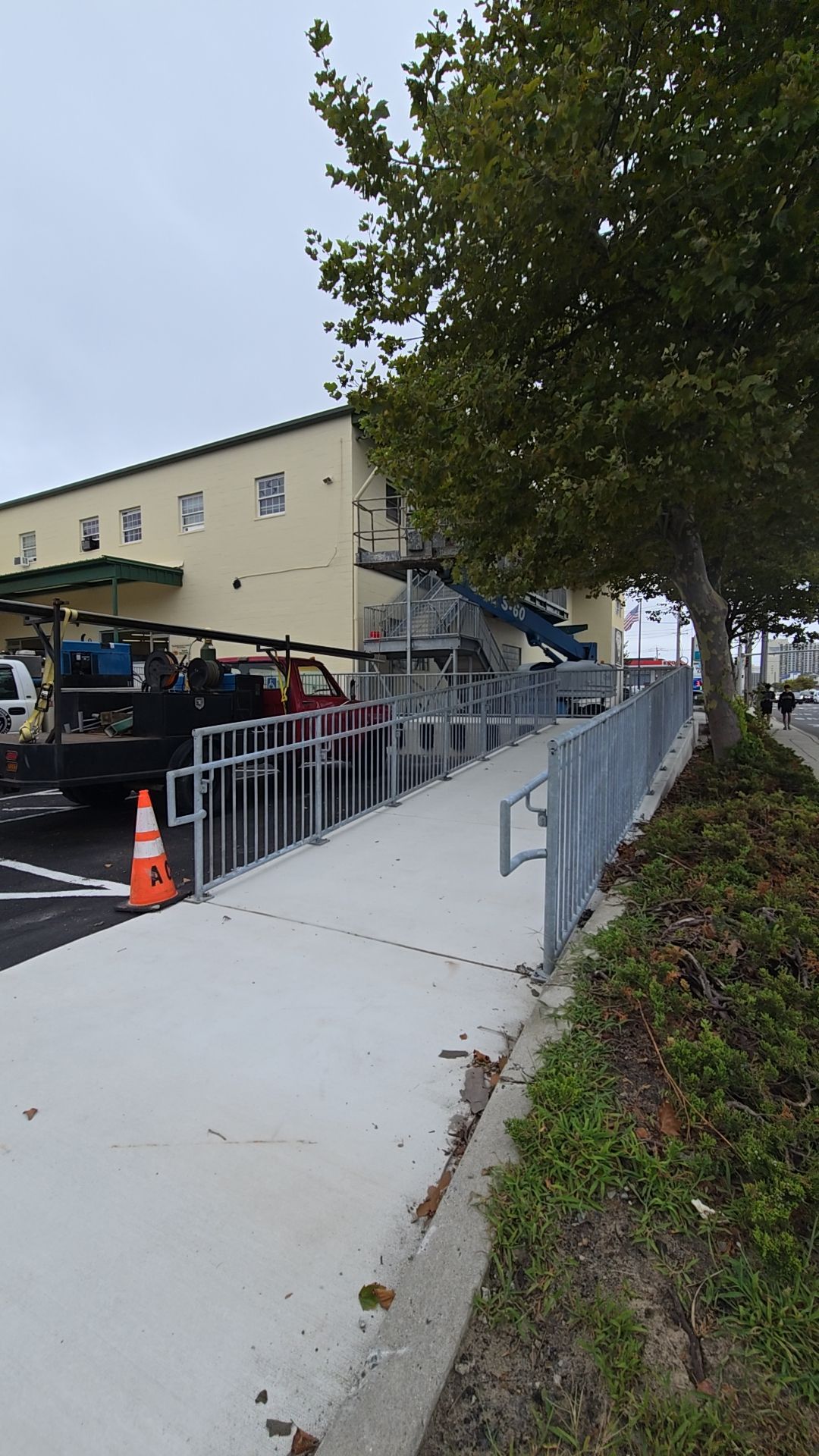 Sidewalk ramp with metal railings leading to a building. A tree is to the right.