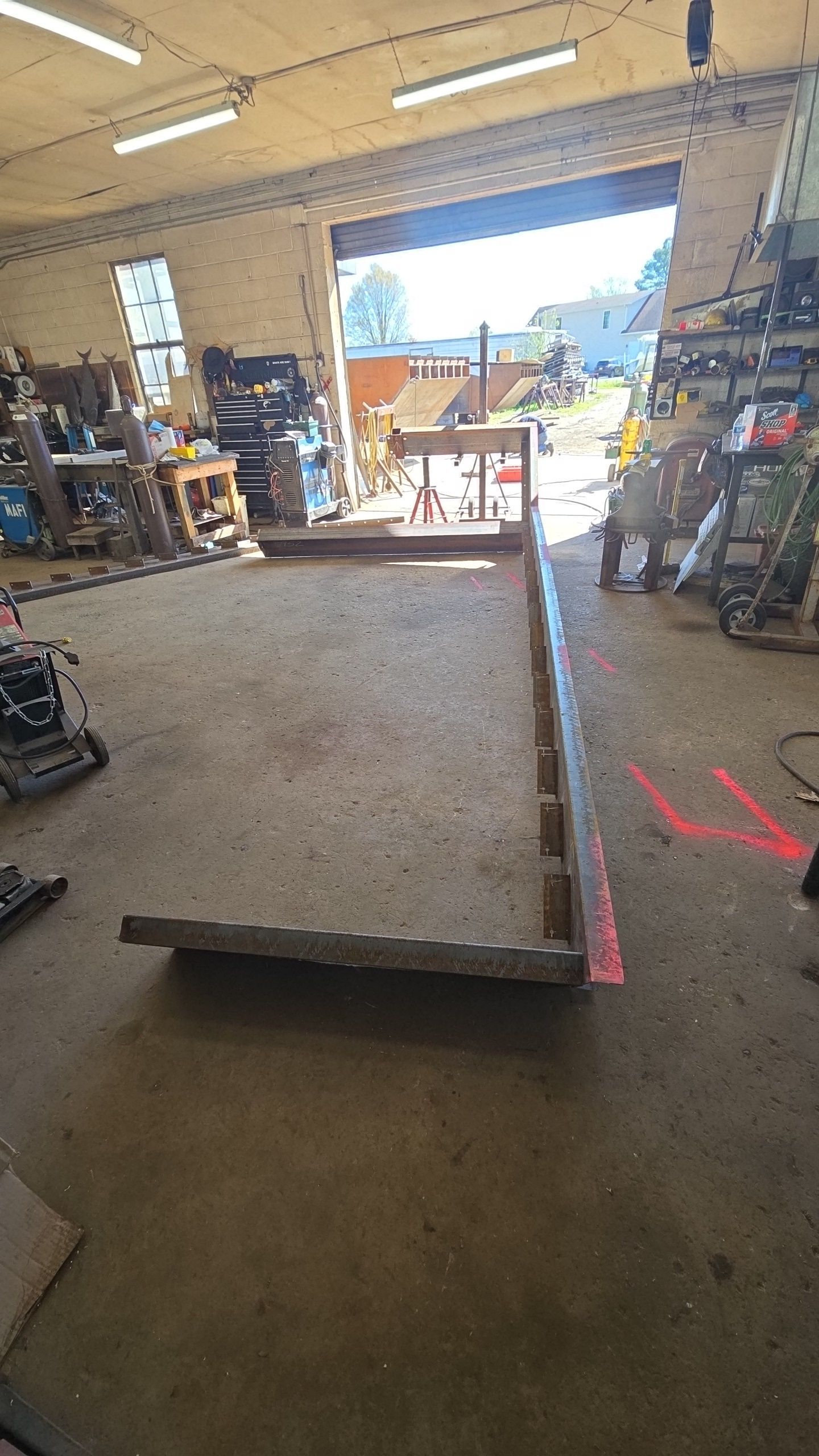 A workshop interior with a concrete slab partially constructed, and a garage door open to the outside.