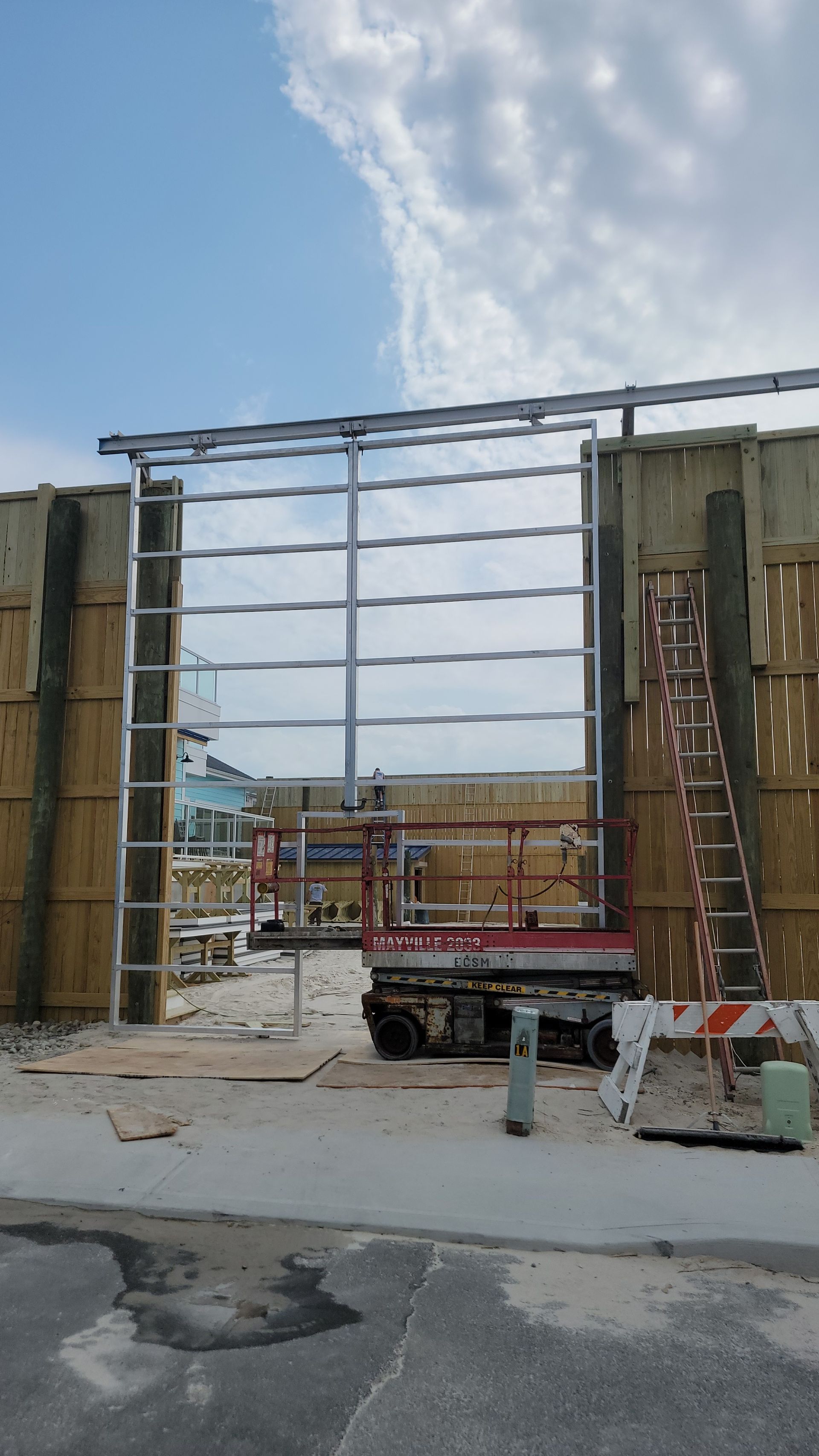Construction site: steel frame, walls, scissor lift, ladder, blue sky.