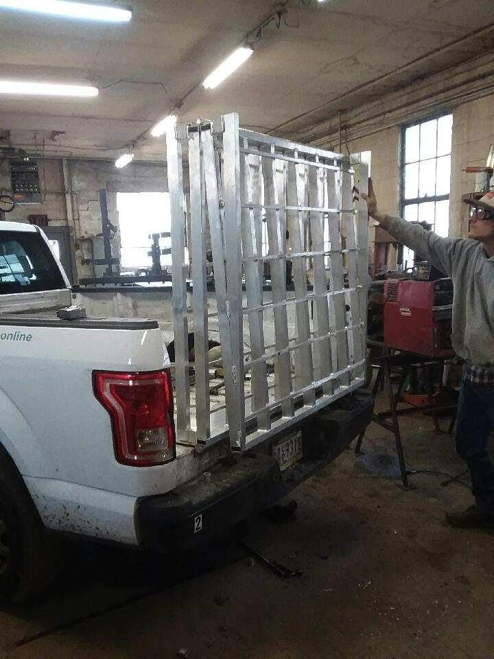 A man loads a large metal cage into a white pickup truck bed in a workshop.