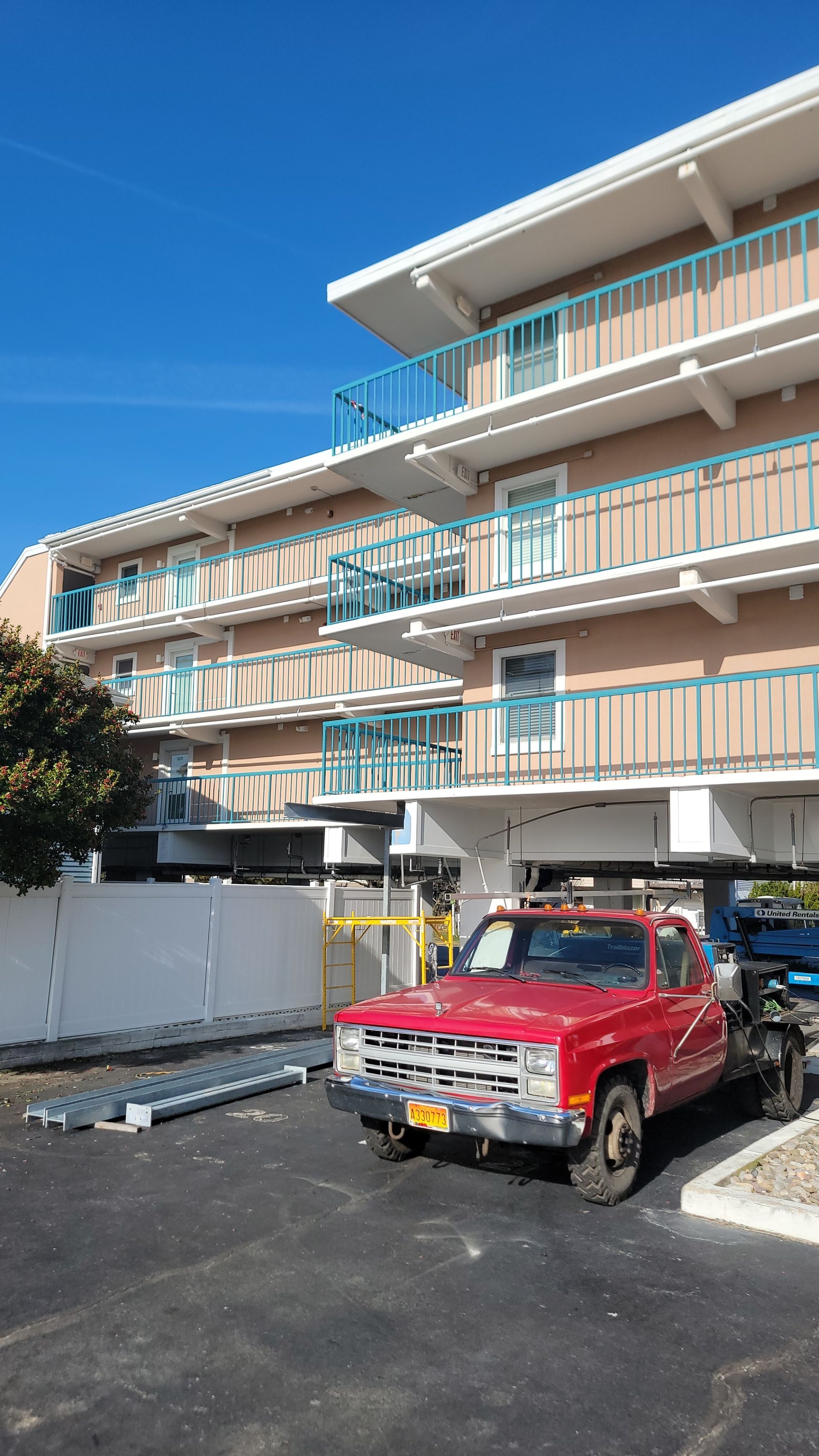 Red pickup truck parked near a multi-story building, which appears to be raised, on a sunny day.