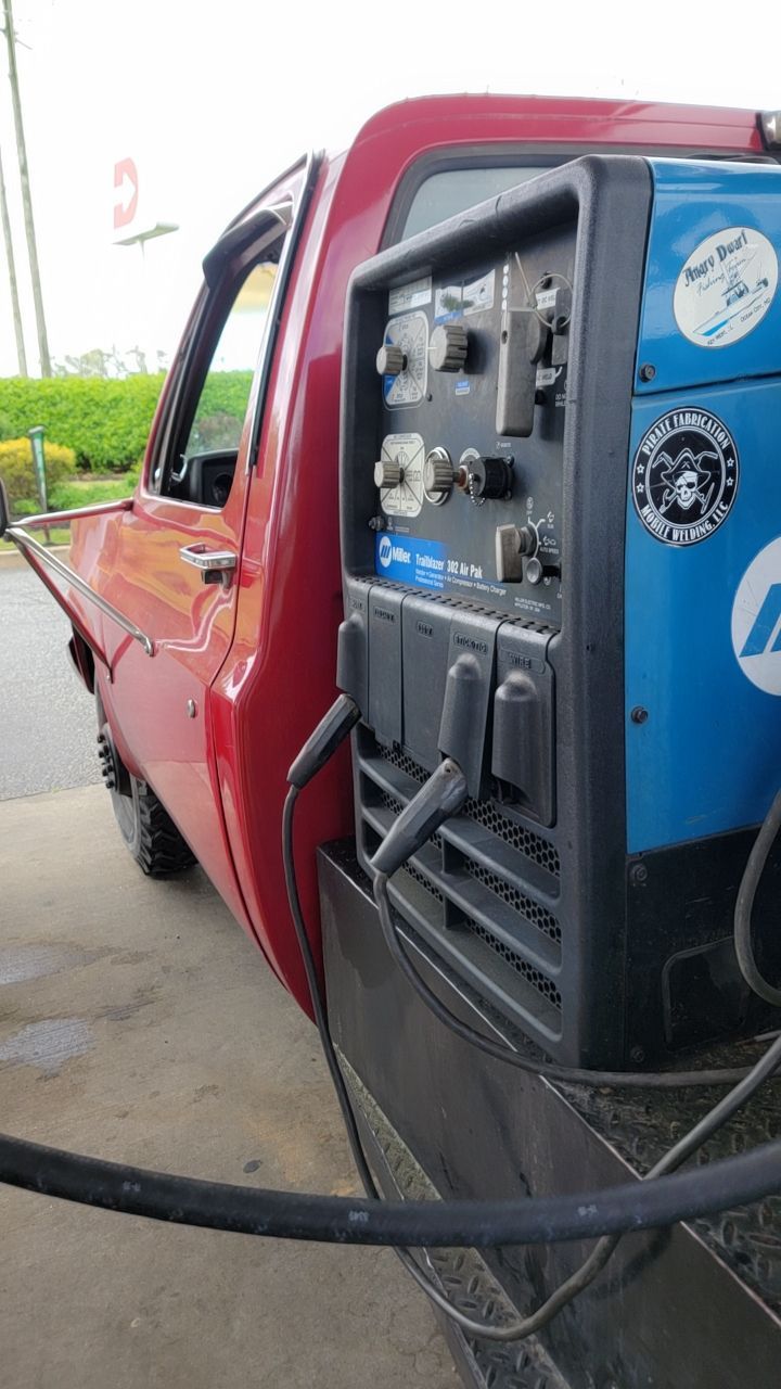 Red pickup truck with a blue Miller welding machine mounted on its side.