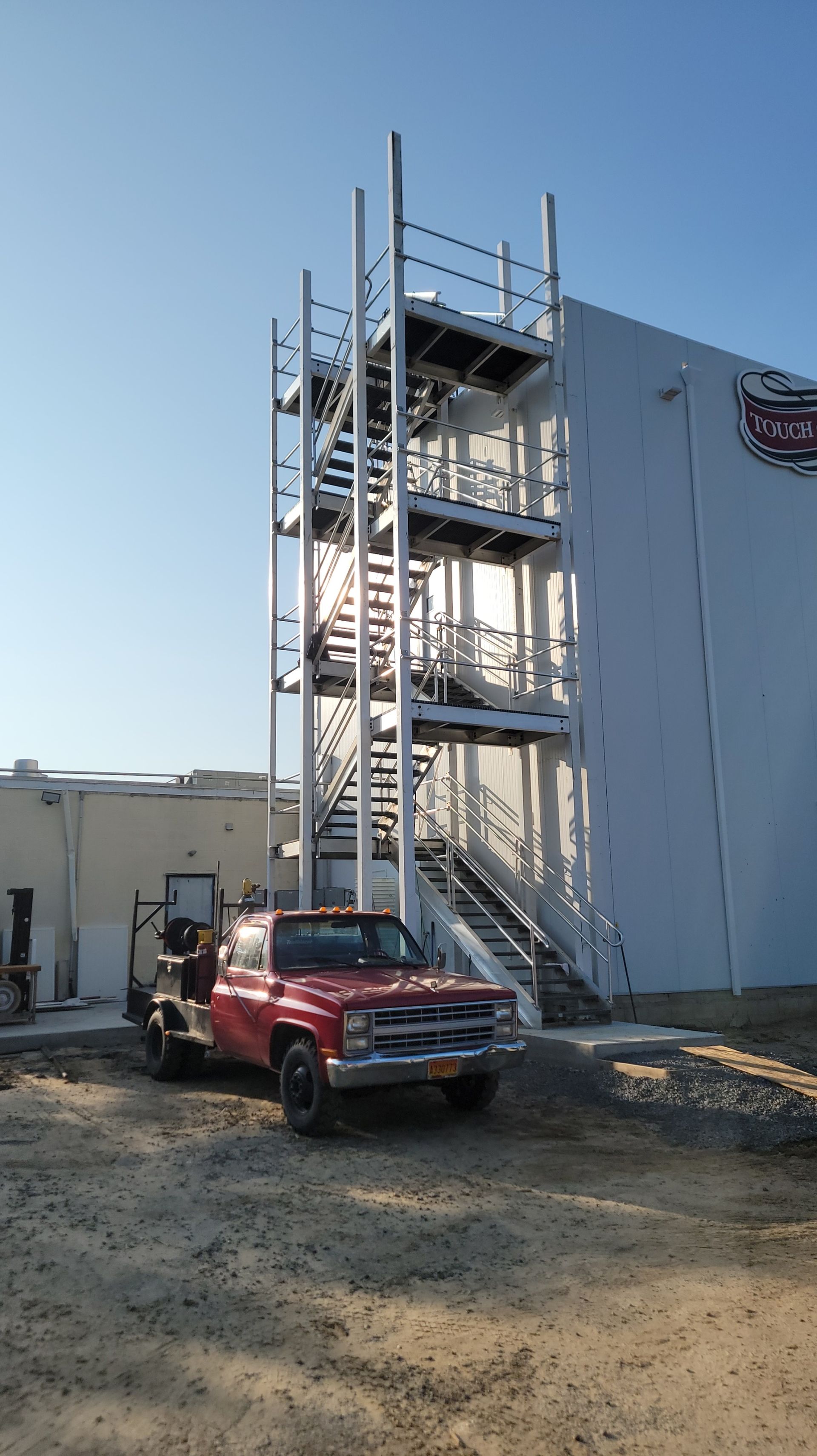 Red truck parked near a white building with an exterior staircase.