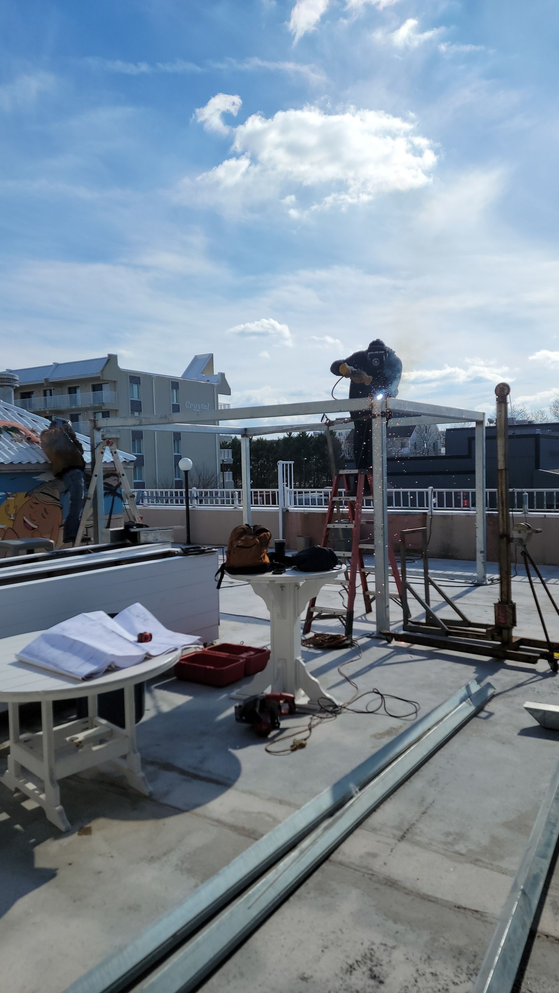 Workers constructing a white metal structure on a rooftop under a partly cloudy sky.
