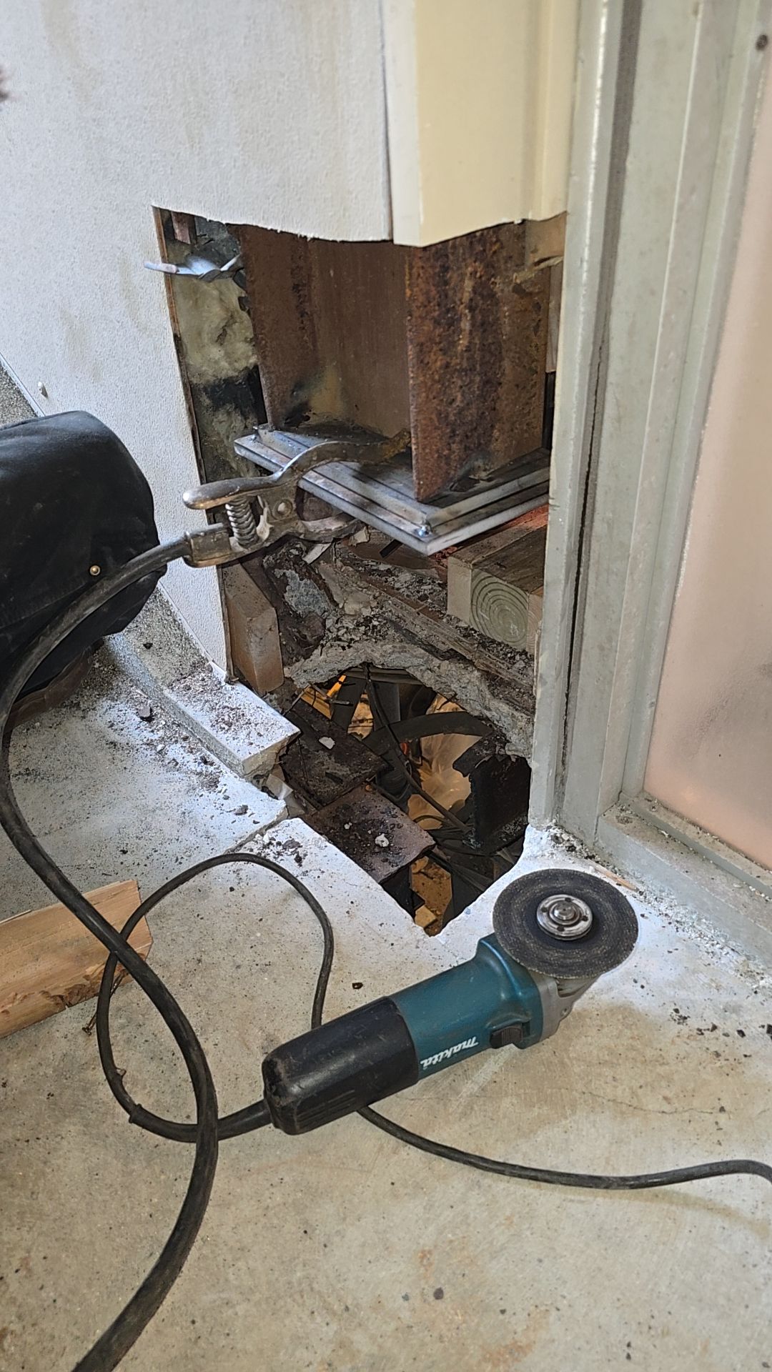 Angle grinder next to a hole cut in a concrete wall. Wires and structural elements are exposed.