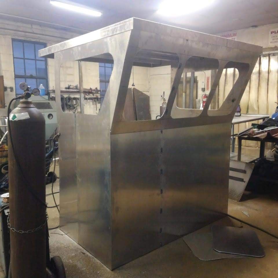 Welded aluminum cabin with window cutouts in a workshop setting.
