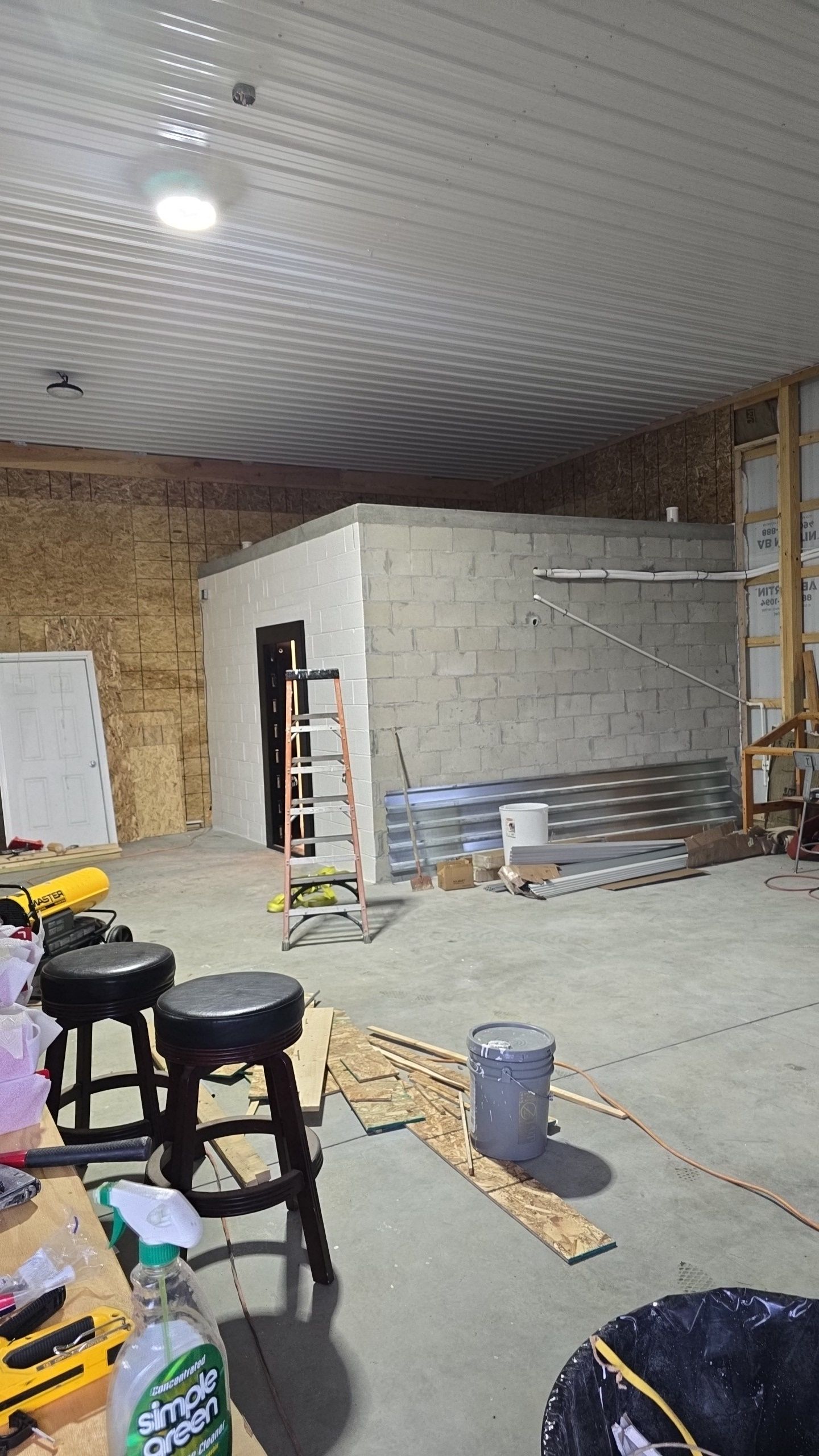 Interior of a garage under construction; cinder block walls, exposed wood framing, construction materials, stools, and a ladder.