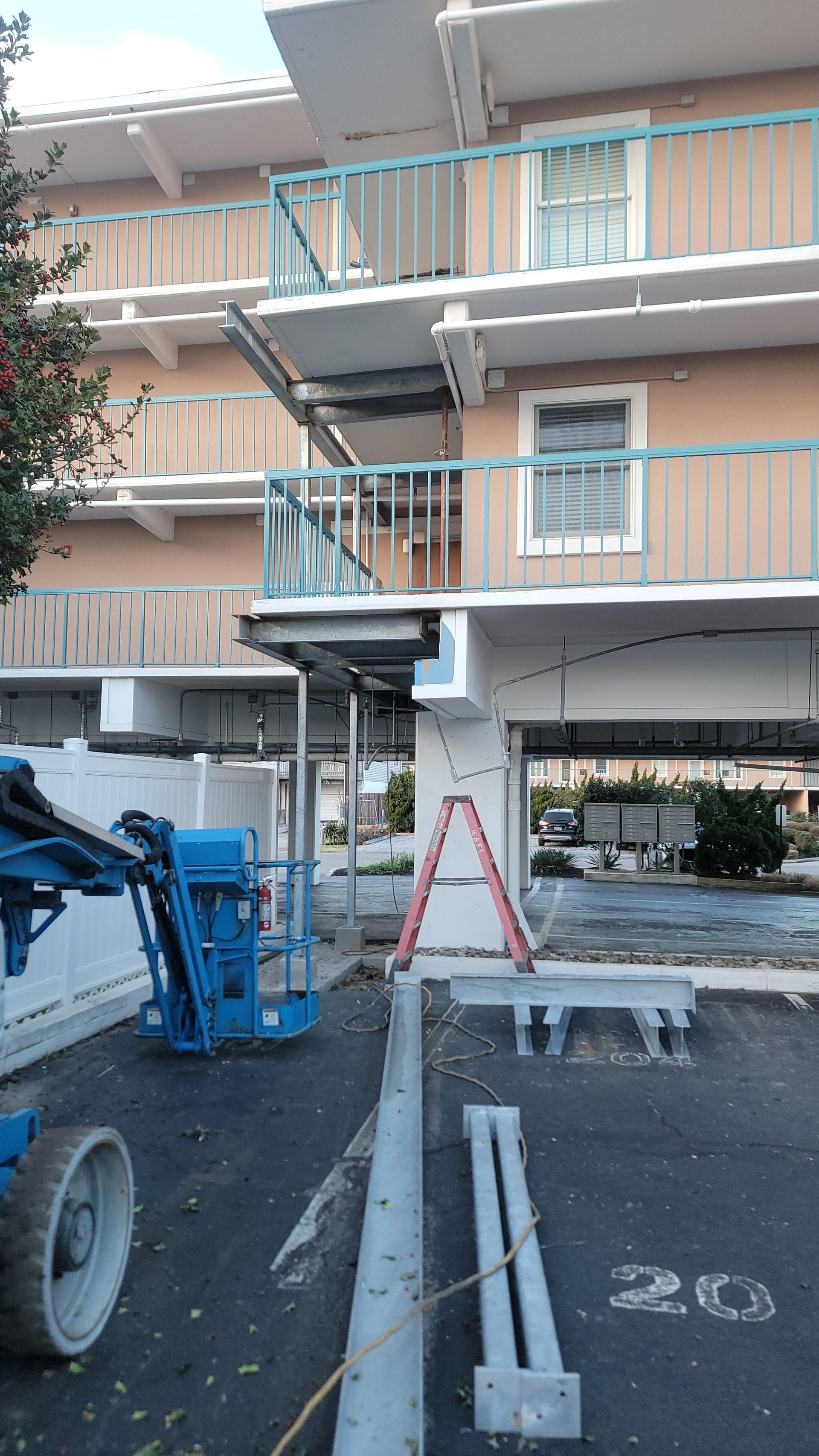 Construction site: scaffolding and lift at a light tan and blue building, some structure removed from the exterior.