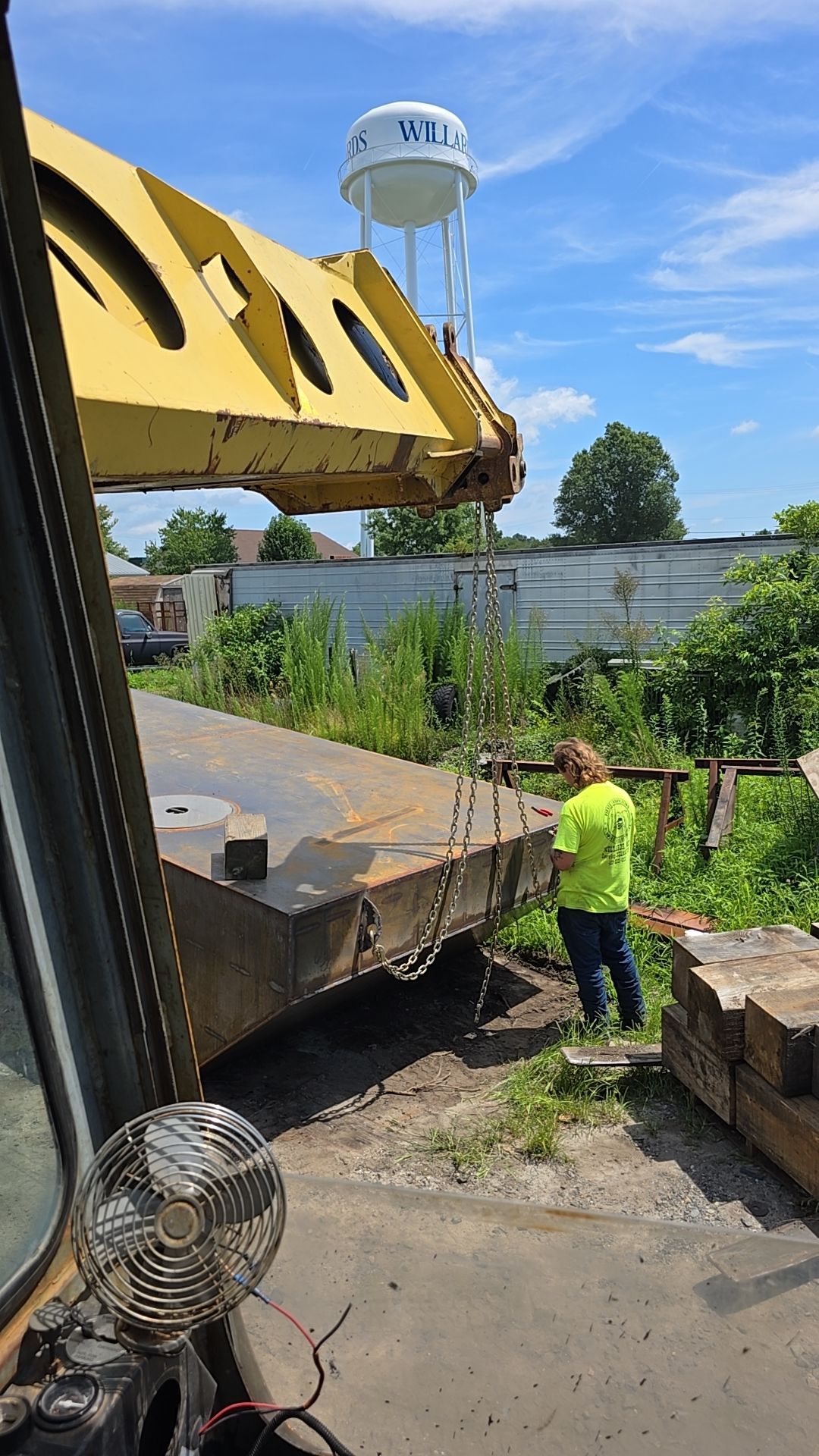 Yellow crane lifting something with a worker in neon green shirt nearby, water tower in background.