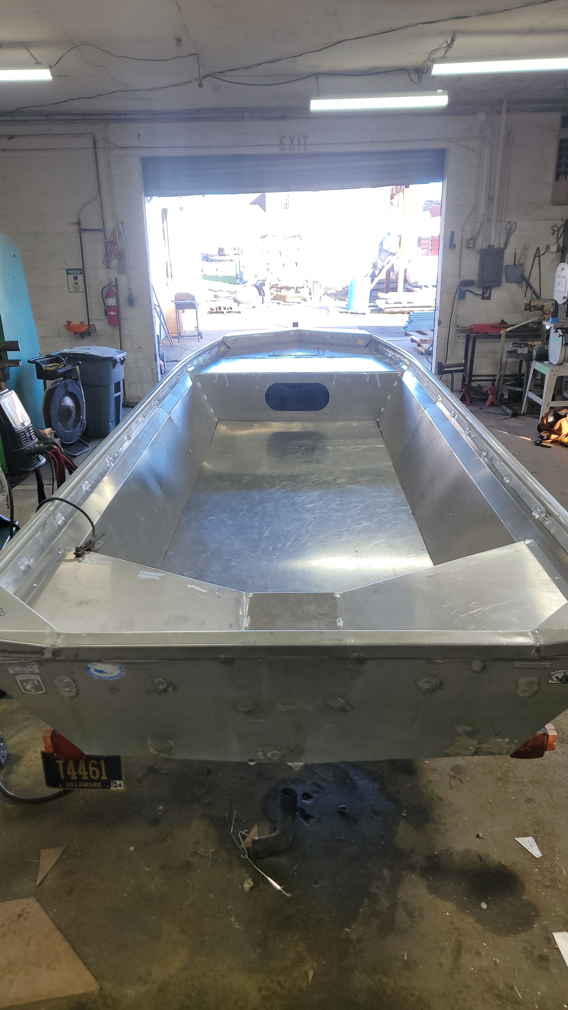 An empty aluminum boat inside a workshop, with an open doorway behind it.