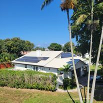 A house with solar panels on the roof and palm trees in front of it.
