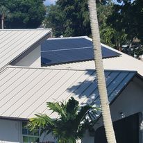 A house with solar panels on the roof and a palm tree in the foreground.