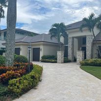 A large white house with a driveway and palm trees in front of it.