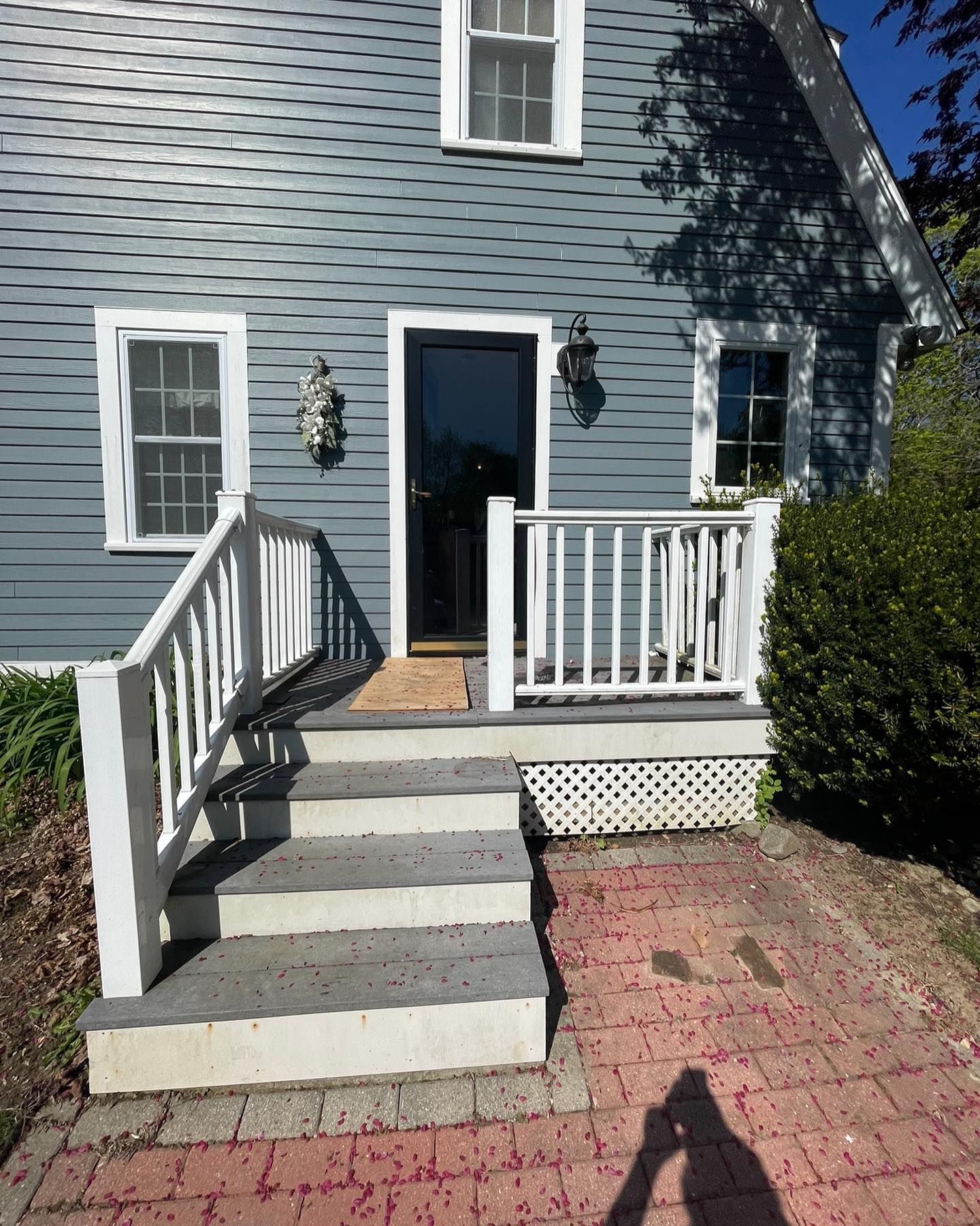 Blue-sided house entrance with a white porch, stairs, railings, and a brick walkway leading to the front door.