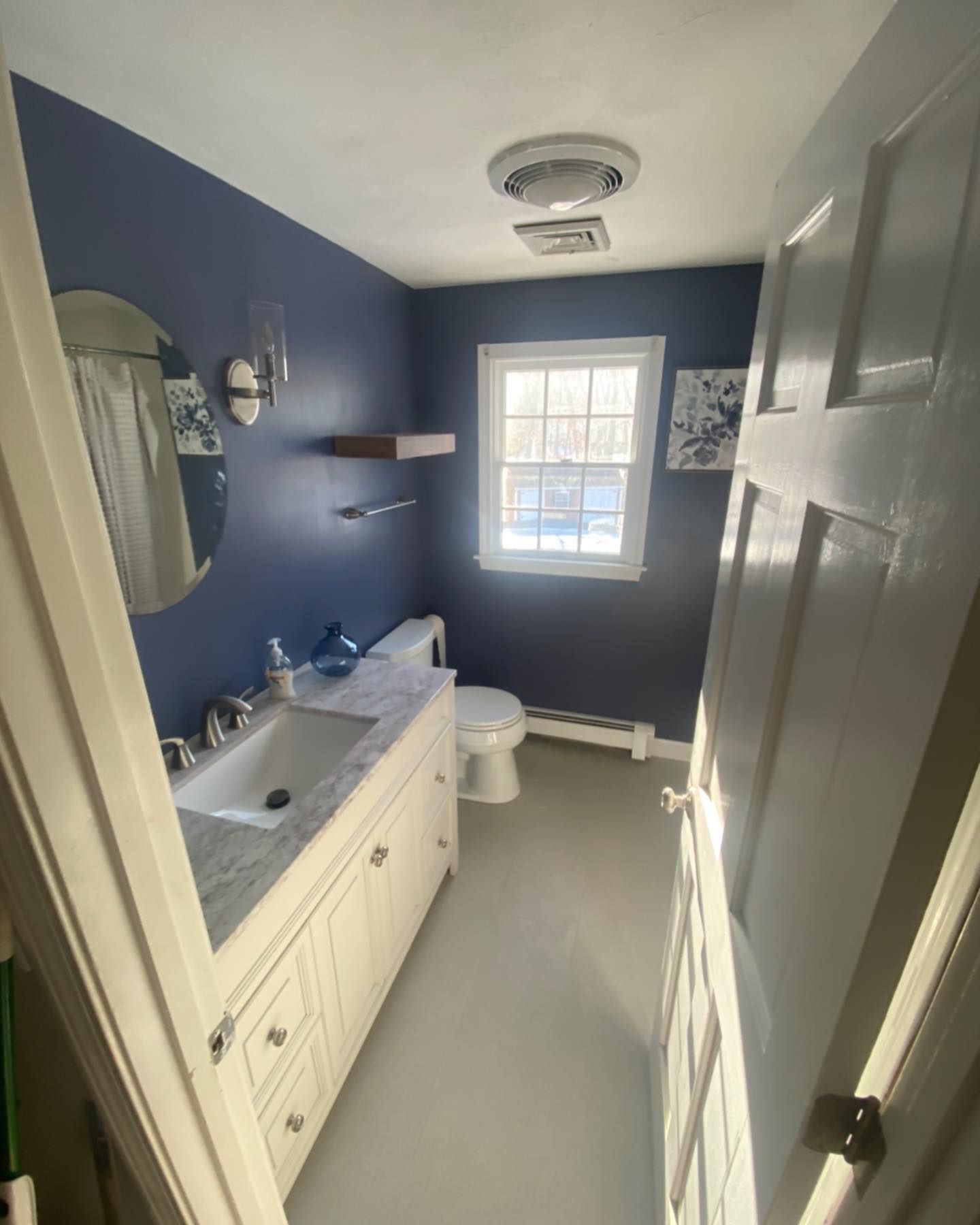 A small, narrow bathroom with dark blue walls, a white vanity with a marble countertop, and a white toilet.