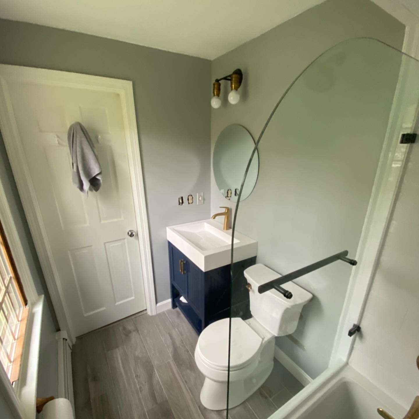 A bathroom with gray walls, a navy blue vanity, a white toilet, and a glass shower partition.