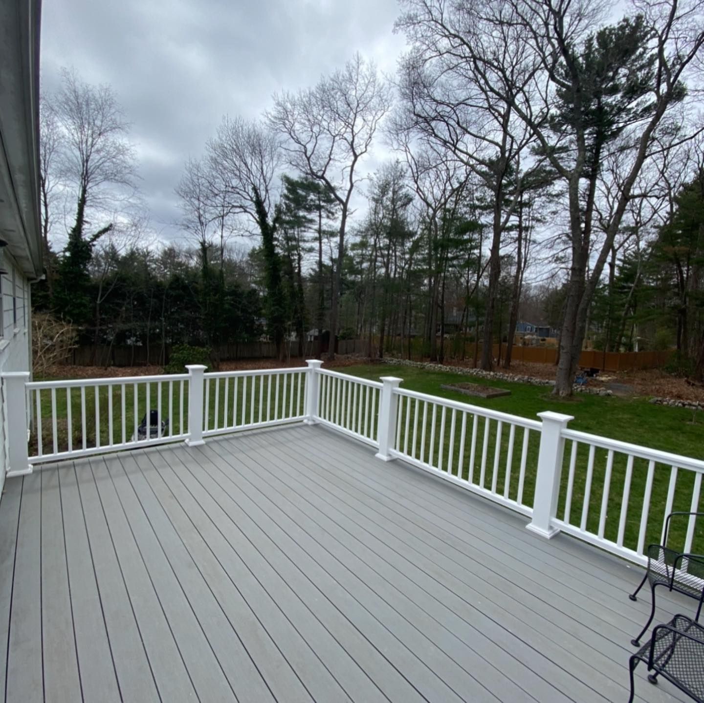 A light gray composite deck with white railings overlooks a grassy backyard surrounded by bare trees under a cloudy sky.