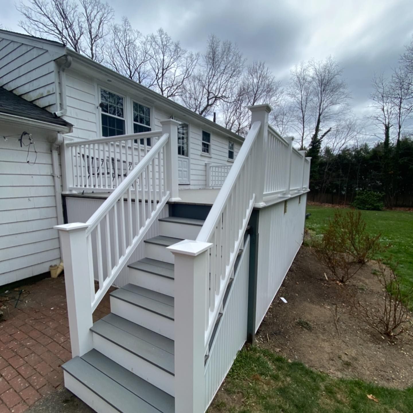 A white wooden deck with stairs leading to a house exterior on a cloudy day.