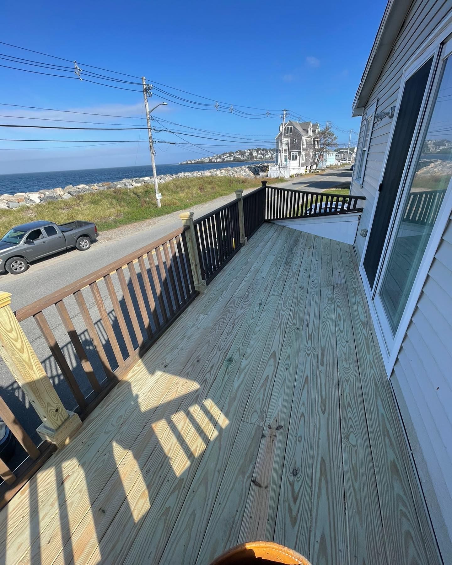 A wooden deck overlooking a coastal road, a parked truck, and the ocean under a clear blue sky.