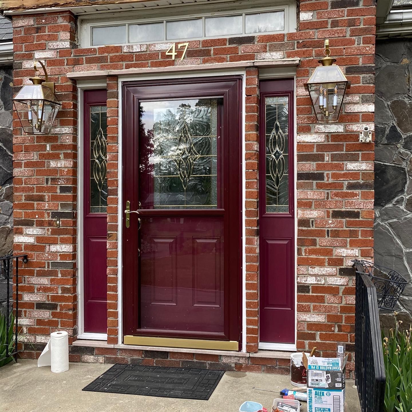 A dark red front door with a glass window and sidelights, set in a red brick wall with two lanterns.