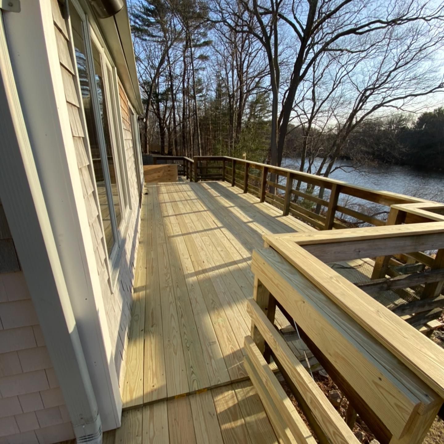 A newly constructed light-wood deck overlooks a river surrounded by bare trees under a clear blue sky.