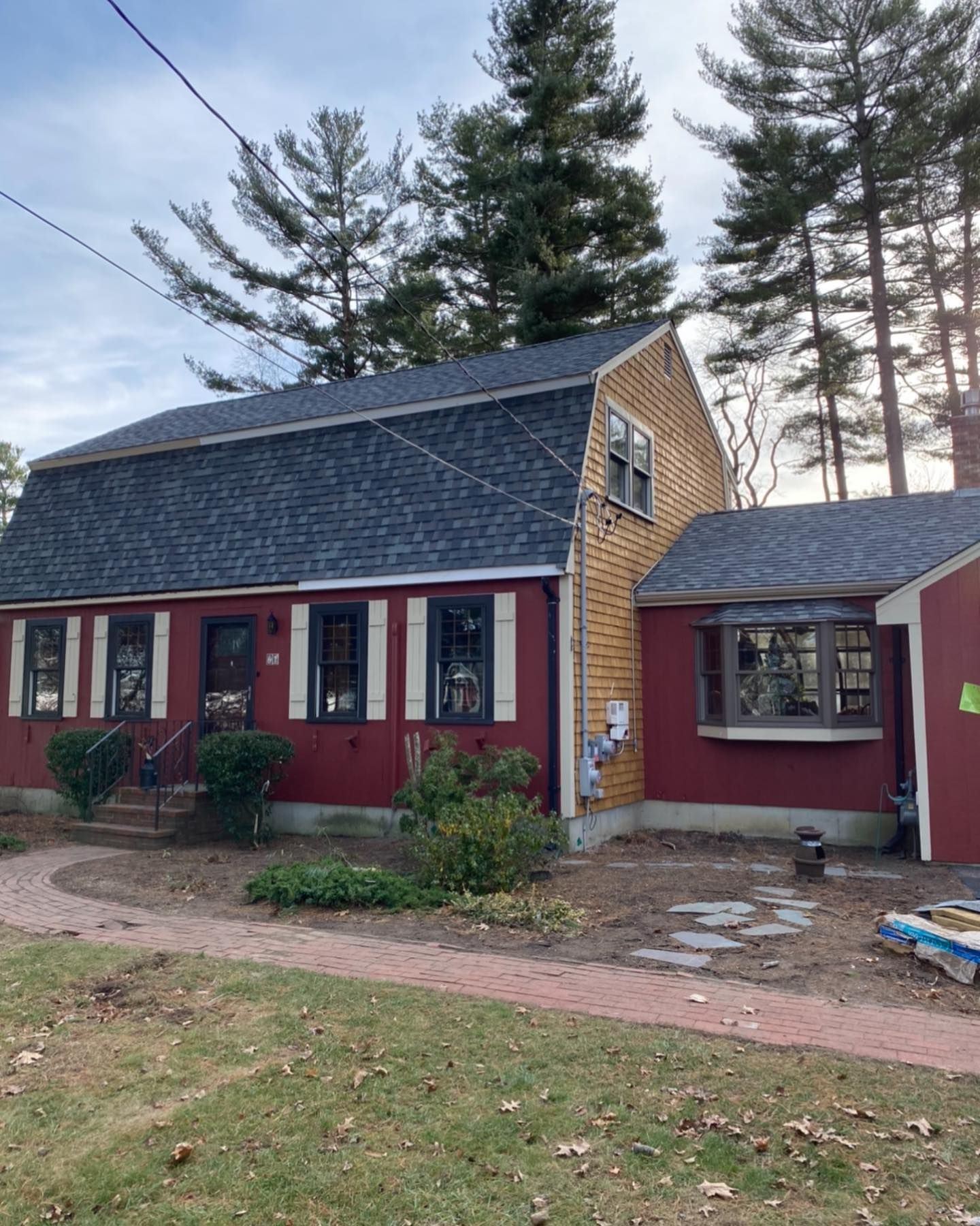 A red Dutch colonial home with a dark shingled roof, brown trim, a bay window, and a brick walkway under a clear sky.