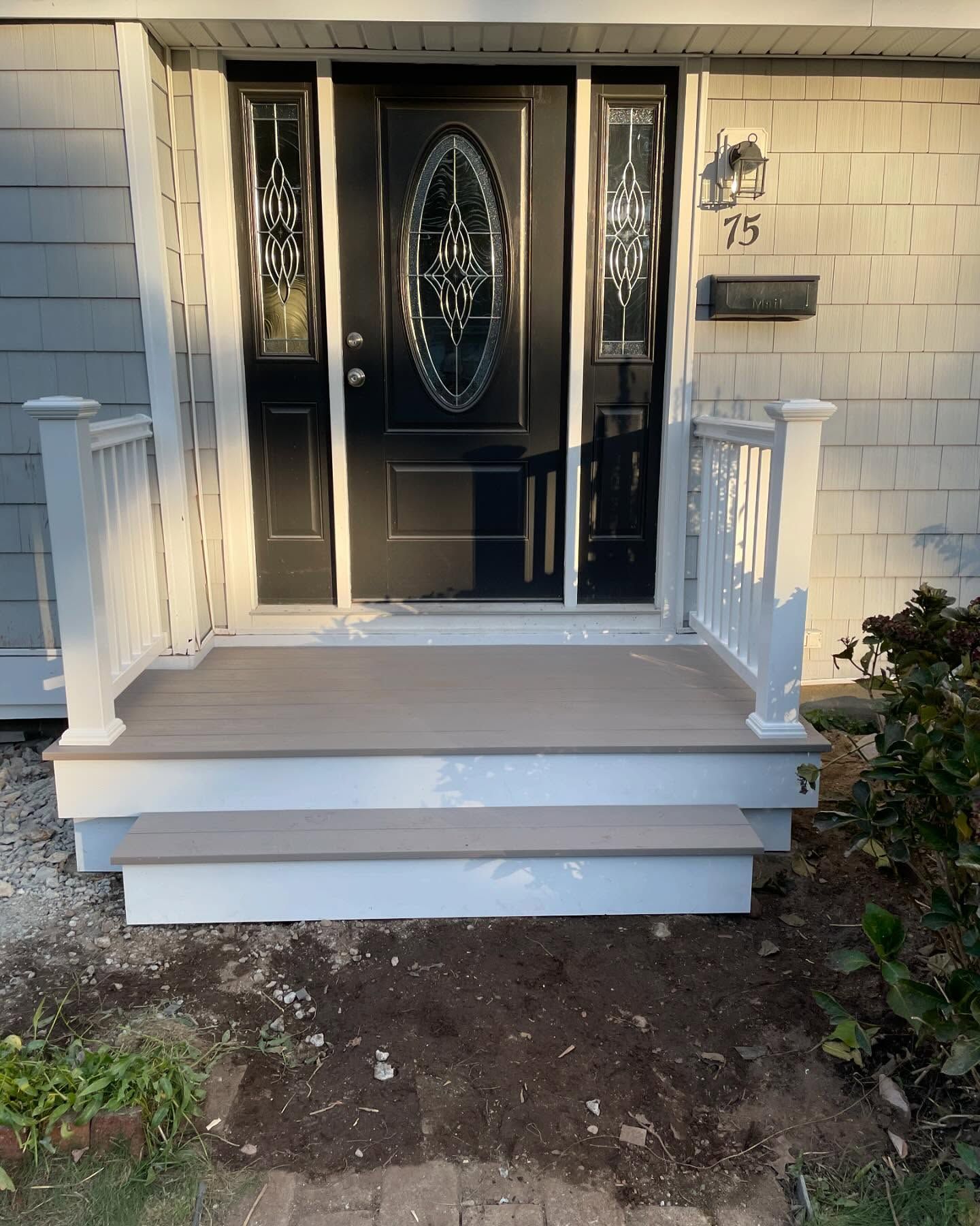 A front entryway with a black oval-glass door, white railings, and a two-step deck with light brown surfaces.