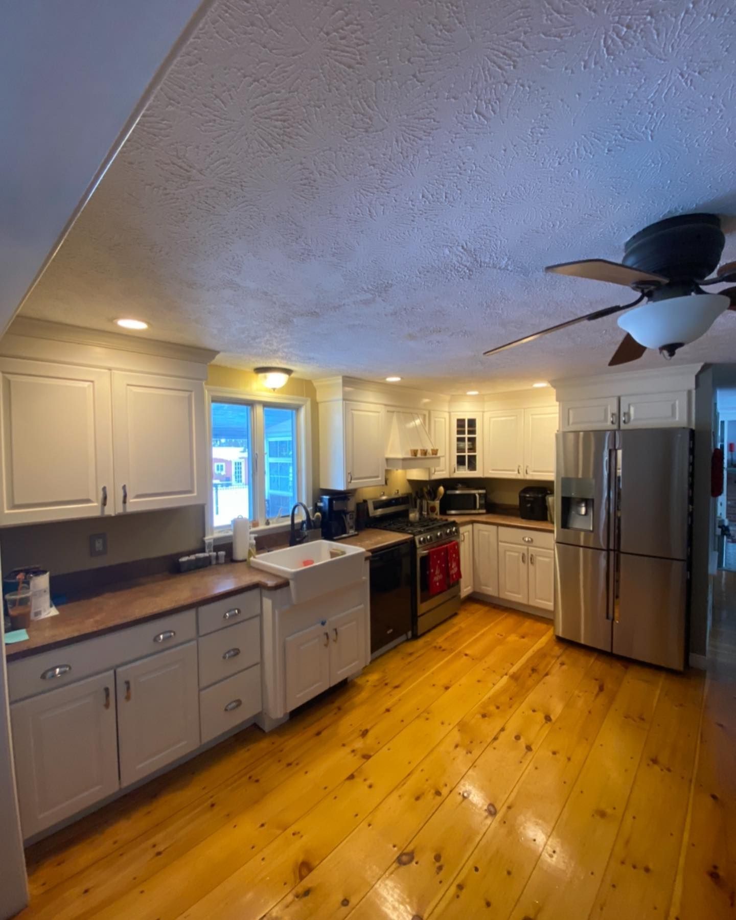 A kitchen with white cabinets, dark wood countertops, stainless steel appliances, and polished natural wood flooring.