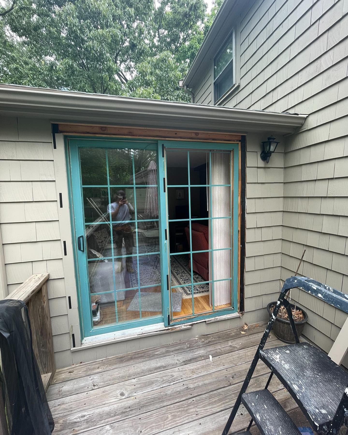 A turquoise sliding glass door installed in a house with light tan shingle siding, viewed from an outdoor wooden deck.