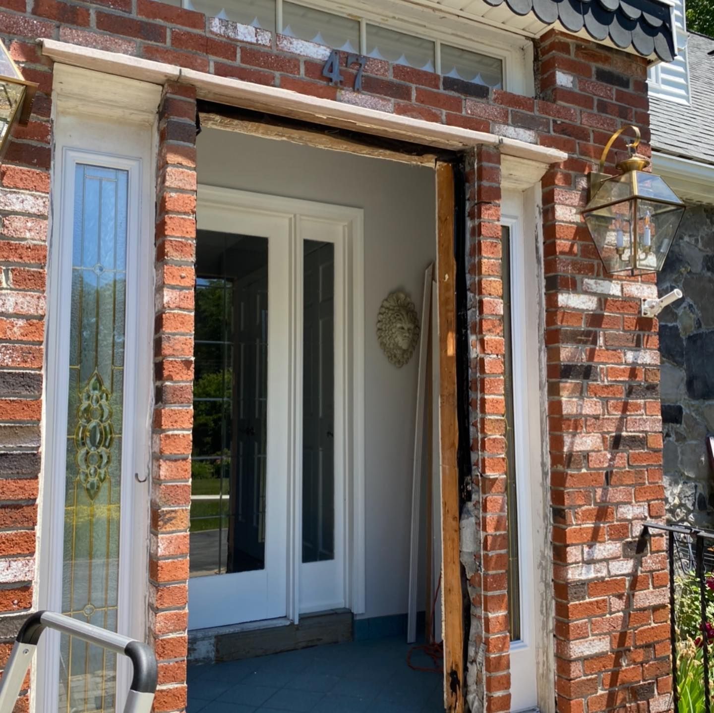 A brick entryway with a removed front door, revealing a white door frame and side lights under a transom window.