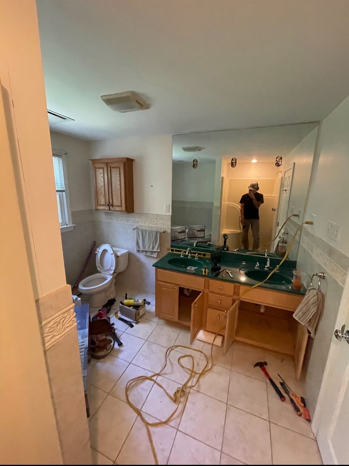 A person works on a bathroom renovation with an open vanity, tools on the floor, and a toilet in the corner.
