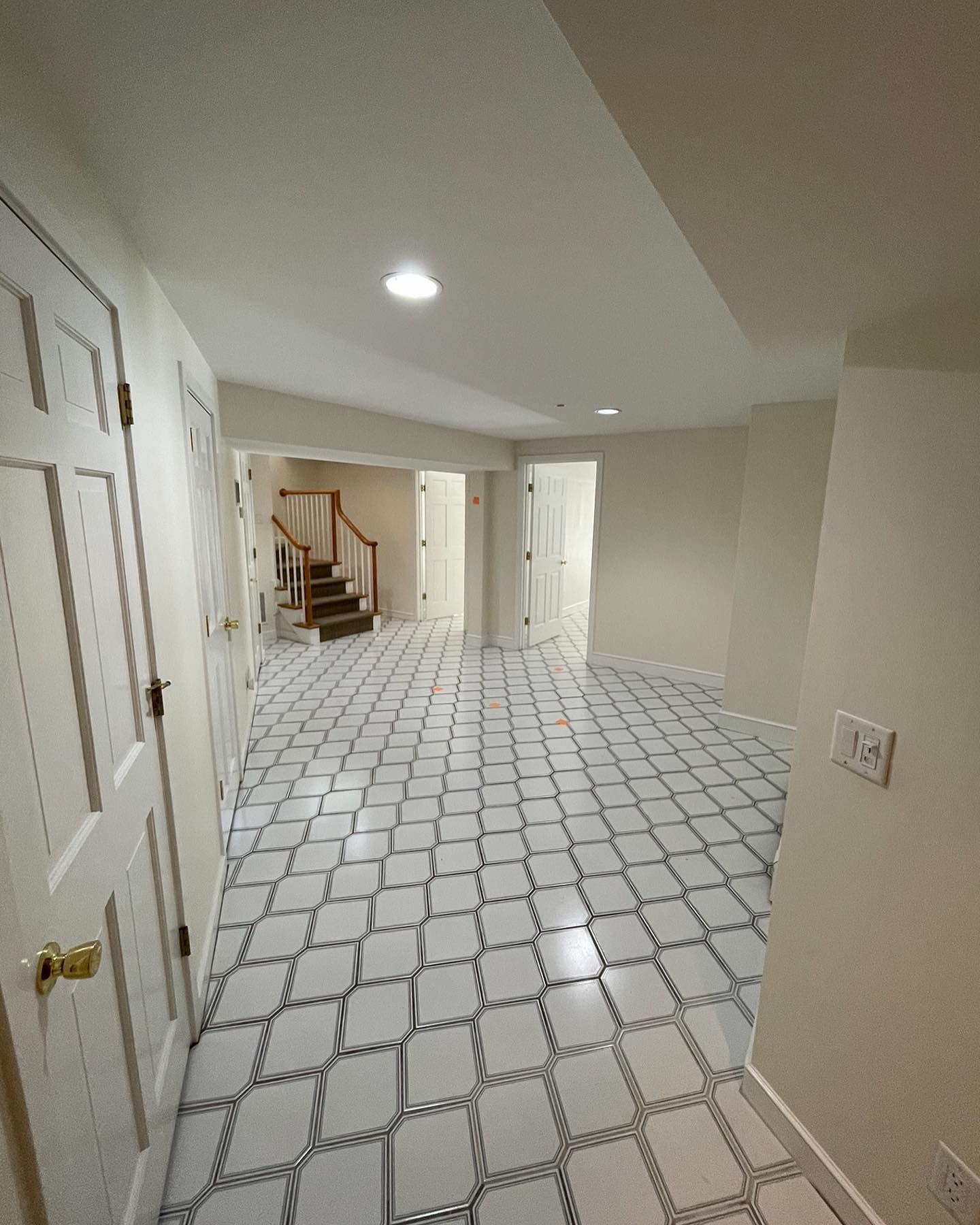 A hallway with a decorative white-and-gray patterned tiled floor, leading toward a staircase and two white doors.