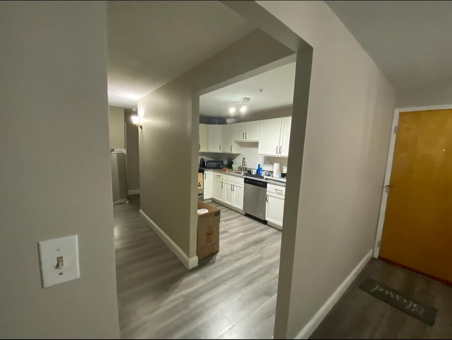 A view from a hallway looking into a kitchen with white cabinets, stainless appliances, and wood-look flooring.