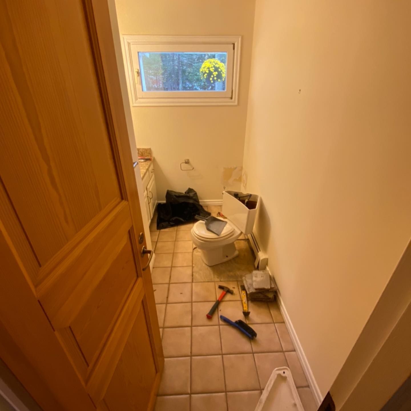 A bathroom undergoing renovation with a detached toilet, tools on tiled floor, and an open door.