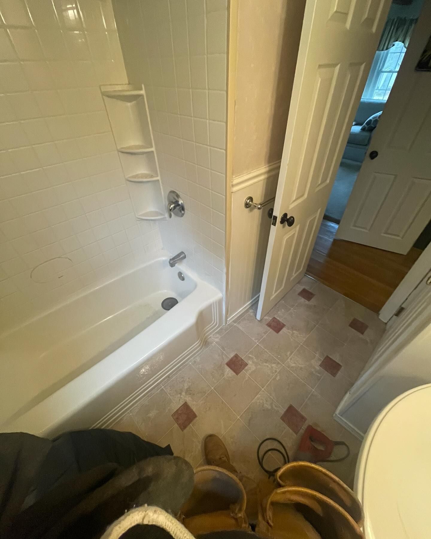 A first-person view of a bathroom showing a white bathtub with integrated shelves, light flooring, and an open doorway.