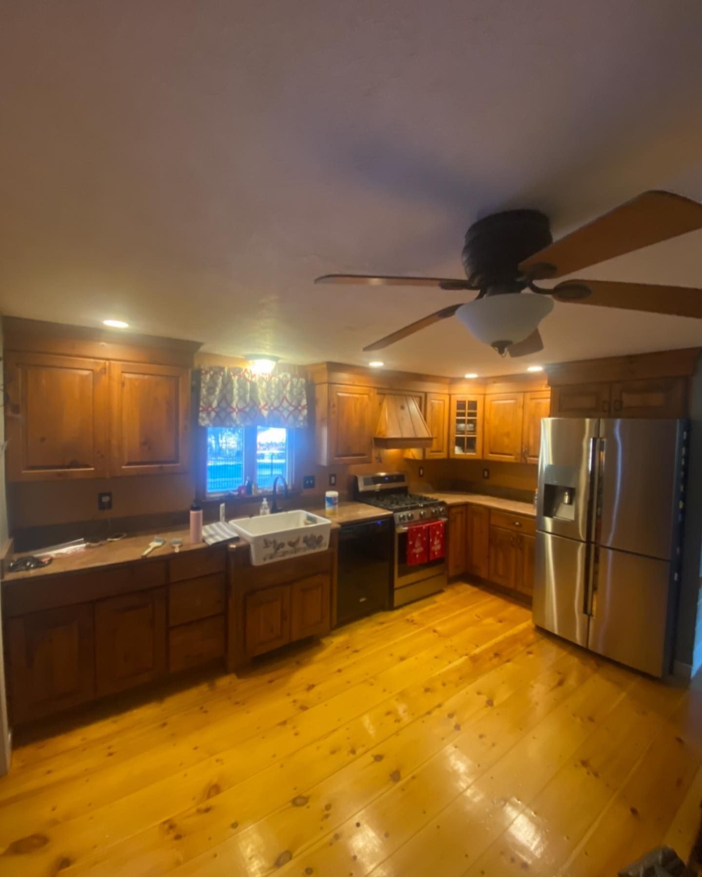 A rustic kitchen with wood cabinets, stainless steel appliances, a farmhouse sink, and light-colored wood flooring.