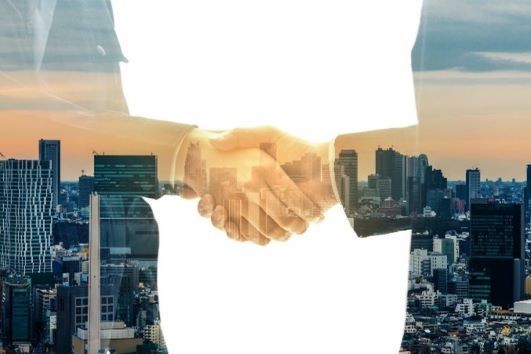 Shapes of two business people shaking hands. While their hands look like hands, their bodies show a city scene