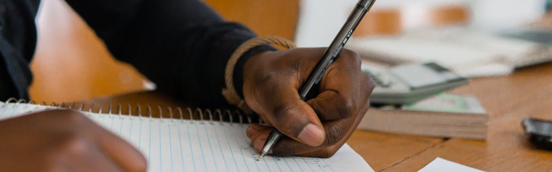 A left-handed Black man writes on a notebook